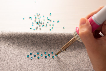 Handmade decoration. A process of soldering rhinestones on a gray cloth by soldering iron