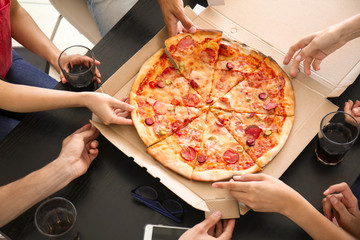 Young people taking slices of hot tasty pizza from cardboard box