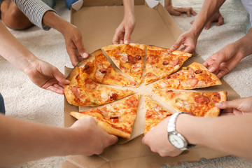 Young people taking slices of hot tasty pizza from cardboard box
