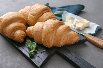 Wooden board with tasty croissants on grey textured background
