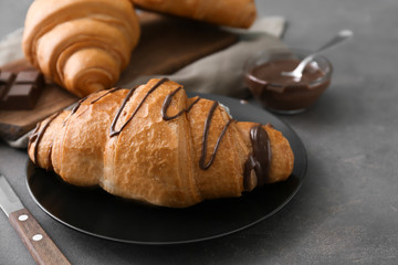 Plate with tasty croissant and chocolate sauce on grey background