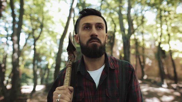 Walking bearded lumberjack with axe. Man in a cap walks through the woods in search of the tree