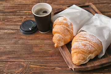 Wooden board with tasty croissants and cup of coffee on table