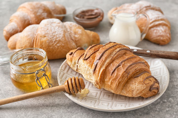 Plate with tasty croissant and honey on grey background