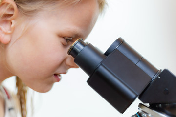 Ein 7 jähriges Mädchen schaut in das Okular eines Mikroskops. Freisteller