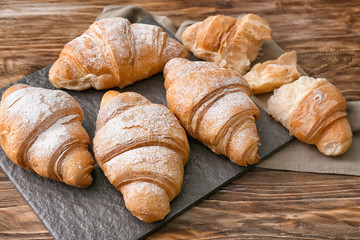 Slate plate with tasty croissants on wooden table