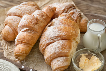 Tasty croissants with milk and butter on wooden table