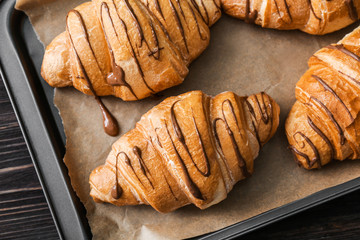Tasty croissants with chocolate sauce on baking tray