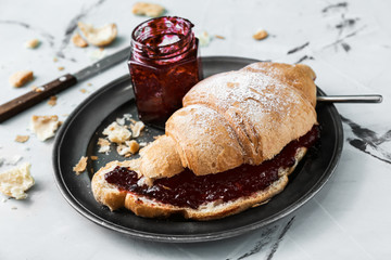 Plate with tasty croissant and jam on table