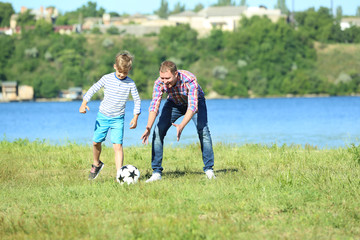 Fototapeta premium Szczęśliwy ojciec i syn grający w piłkę nożną w pobliżu rzeki