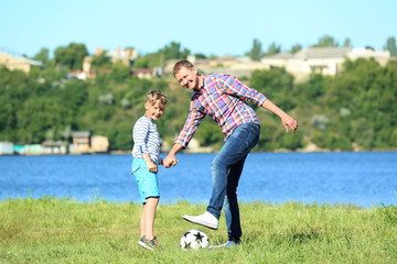 Obraz premium Happy father and son playing football near river