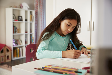 Young Girl Sitting At Desk In Bedroom Doing Homework
