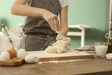 Obraz na płótnie Canvas Woman sprinkling flour on dough in kitchen