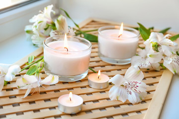 Fototapeta na wymiar Burning wax candles with flowers on windowsill