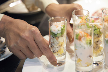 Crop close-up view of bartender hands serving glass cocktail shots filled with chopped bright delicious fruits 