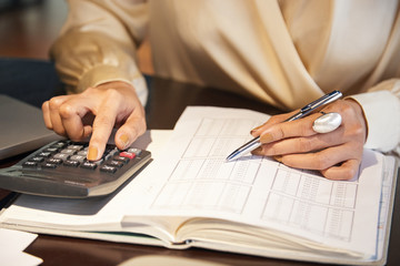Crop view of elegant female hands with ring holding metal pen and using calculator to account income from chart in notebook
