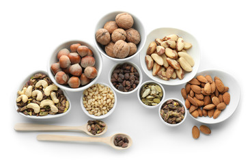 Bowls and spoons with different nuts on white background