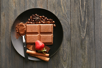 Plate with tasty milk chocolate and strawberry on wooden background