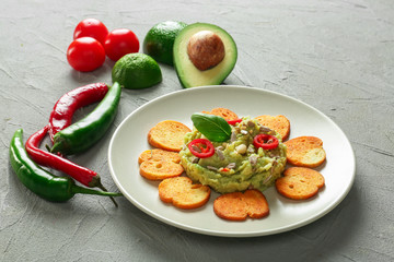 Plate with tasty guacamole, rusks and fresh vegetables on textured background