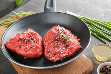 Frying pan with raw meat, herbs and spices on wooden board
