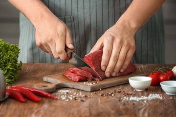 Man cutting raw meat on wooden board in kitchen