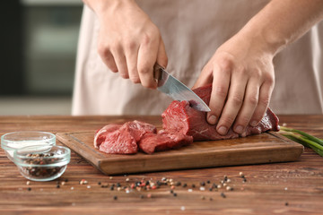 Man cutting raw meat on wooden board in kitchen