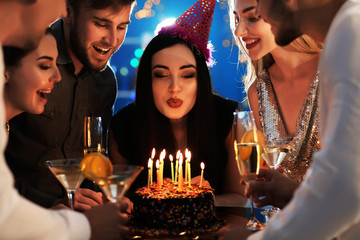 Young woman blowing out candles on her birthday cake with friends in club
