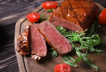 Wooden board with tasty grilled steak on table