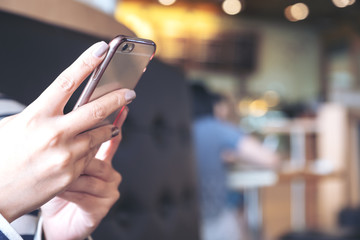 Closeup image of a woman's hands holding , using and looking at smart phone in cafe with blur background