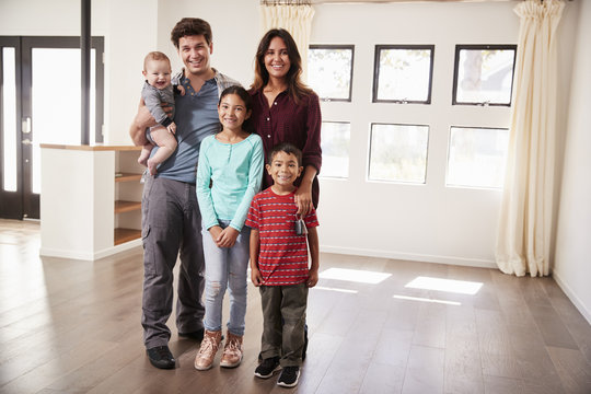 Portrait Of Happy Family With Baby Standing In Empty Lounge Of New Home