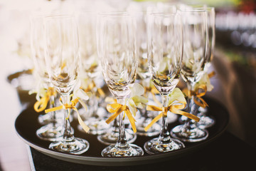 Selective focus on a tall wine glasses decorated with gold ribbon on the tray with light from the back