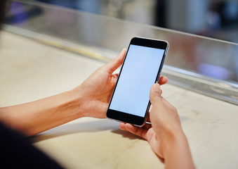 Close up woman hands holding mobile smartphone with white blank screen on the table.