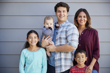 Obraz premium Portrait Of Happy Family With Baby Standing Outside Grey Clapboard House