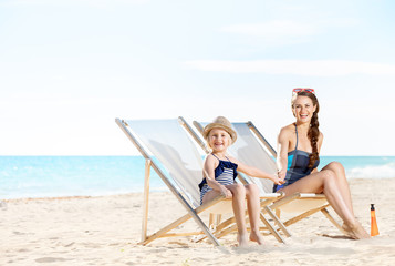 happy mother and daughter on seashore sitting on beach chairs