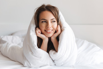 Happy young woman laying in bed covered