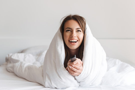 Laughing young woman laying in bed covered in blanket