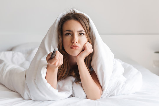Bored young woman laying in bed covered in blanket
