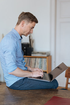 Young man perched on a table with his laptop