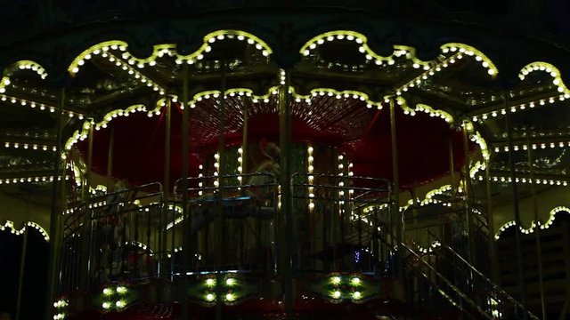 Bright red and golden carousel with horses and bright glowing lights turning around without passengers in darkness of night. Real time full hd video footage.