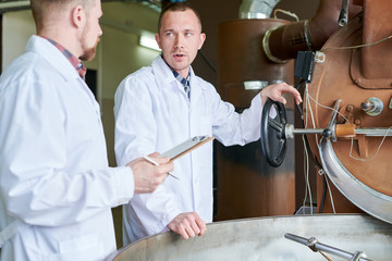 Waist up portrait of two workers wearing lab coats discussing coffee processing while standing by roasting machine, copy space