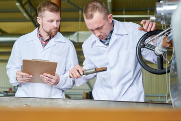 Waist up portrait of two factory workers wearing lab coats discussing coffee processing while...