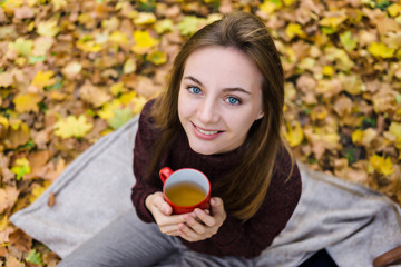 Young woman in the autumn park holds red tea cup