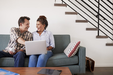 Senior Couple Sitting On Sofa At Home Using Laptop Together