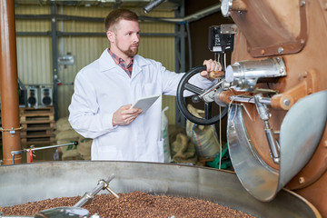 Waist up portrait of modern worker wearing lab coat using digital tablet while working in coffee production manufactory