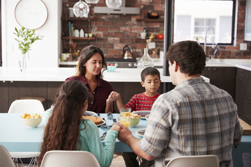 Family Praying Before Meal Around Table At Home