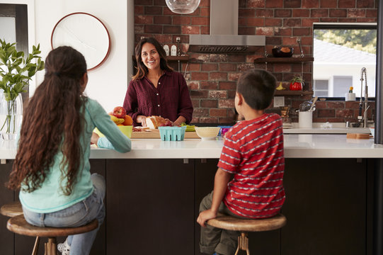 Mother Making School Lunches For Children In Kitchen At Home