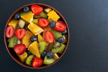 Bowl of healthy fresh fruit salad on dark background. Top view.