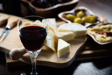 Pouring red wine into the glass above the table set with grape cheese appetizers