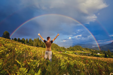 A happy man enjoys the rainbow in the mountains.