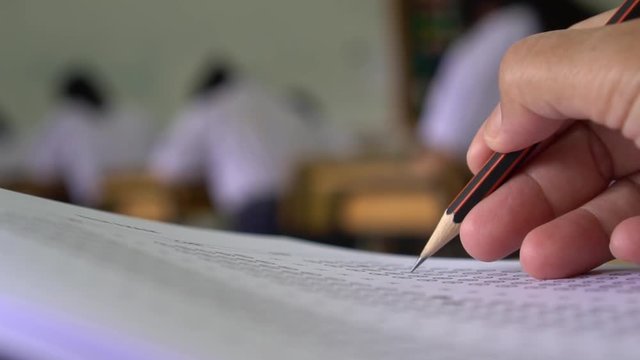Hands with pencil over application form, Students taking exams, writing examination room with undergraduate students inside. Student sitting learning lessons doing final exam in classroom.